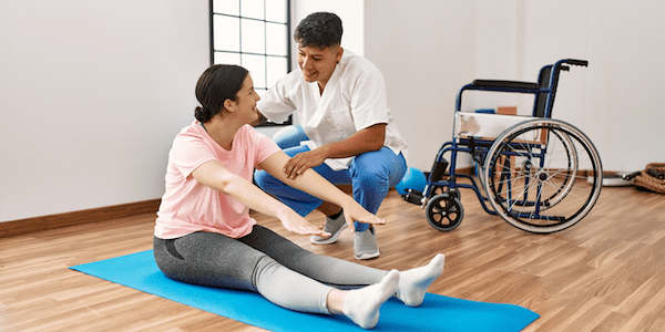 A physical therapist who is also certified in yoga therapy helps a patient stretch, demonstrating the benefits of both yoga and physical therapy.