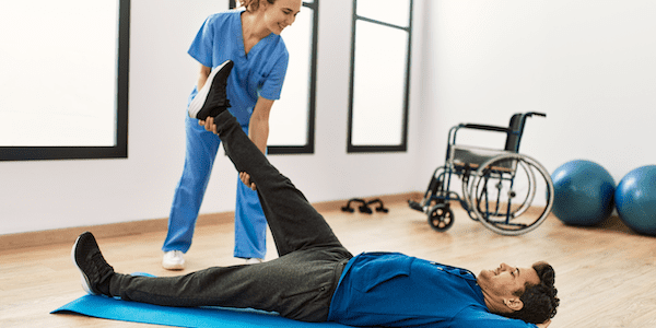 A yoga therapist helps a man stretch on the floor, using yoga therapy for muscular dystrophy clients.