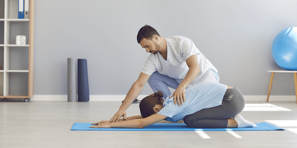 A yoga therapist on the job helping a client with a yoga pose in a clinical setting.