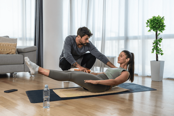 A yoga therapist helping a client with an asana. A furnished space such as this is one of the costs to become a yoga therapist with a private practice.