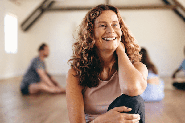 A yoga teacher smiling in her studio. Many yoga teachers ask how much does it cost to become a yoga therapist if they're thinking of advancing their career.