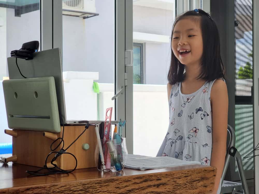 A girl smiling in front of a computer where she can access our online yoga for children's mental health