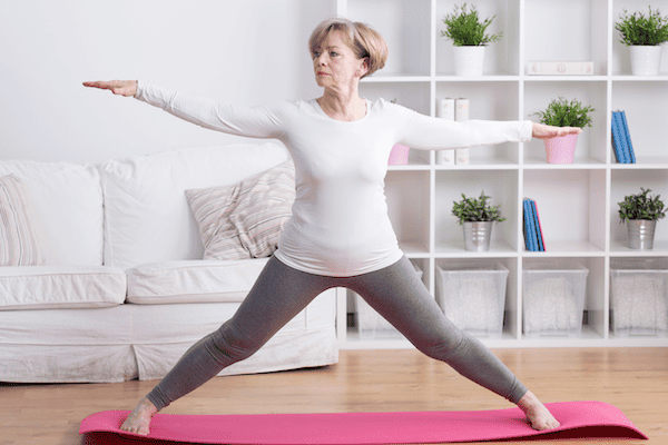 A middle-aged woman who has considered yoga vs Pilates for back pain practices a neutral standing pose