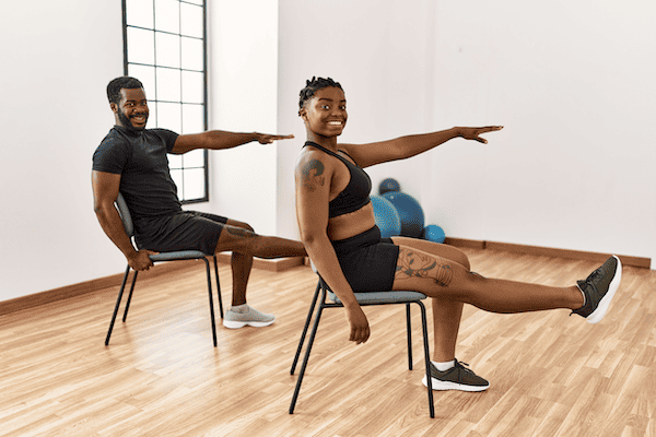A young Black man and a young Black woman practicing chair yoga for weight loss