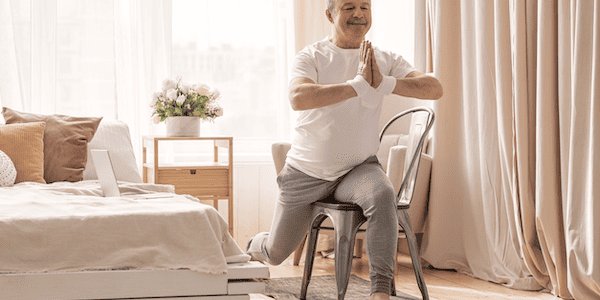 An older man uses a chair for balance and support while stretching, showing that chair yoga is good for weight loss and mobility