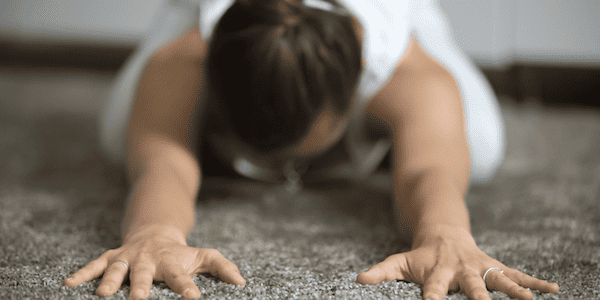 A young woman in Child's Pose on her carpet, bringing up a question that many people have—can you do yoga on carpet?