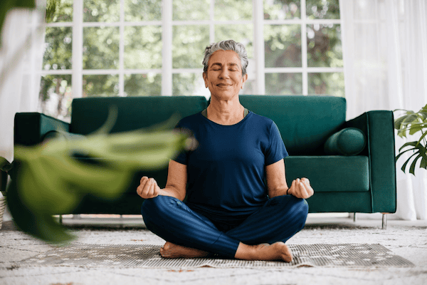 A calm-looking woman cross-legged on the floor practicing yoga for menopause hot flashes