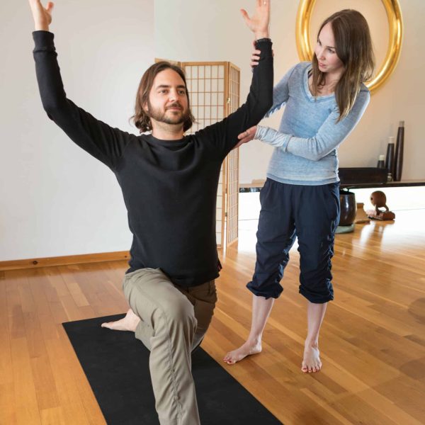 An instructor lifts the arm of a student in a warrior pose.